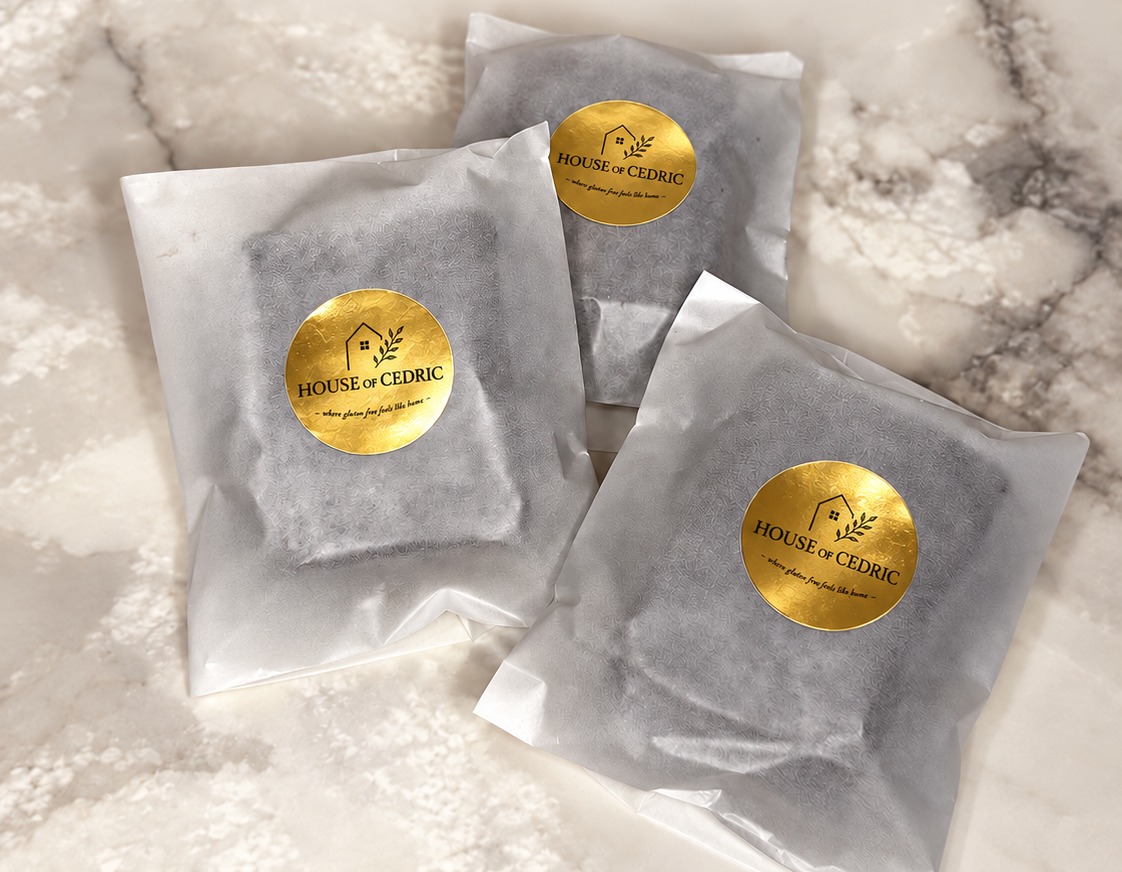 Three House of Cedric brownies wrapped in translucent white paper, each sealed with a gold logo sticker, on marble